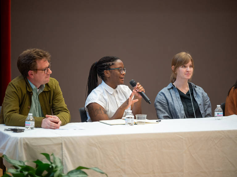 Cassandra Mensah speaks into a microphone during the panel “Documenting the Good Fight: How LDF Stories Are Selected, Collected, and Preserved” while seated next to fellow panelists Jesse Paddock and Susie Penman. 